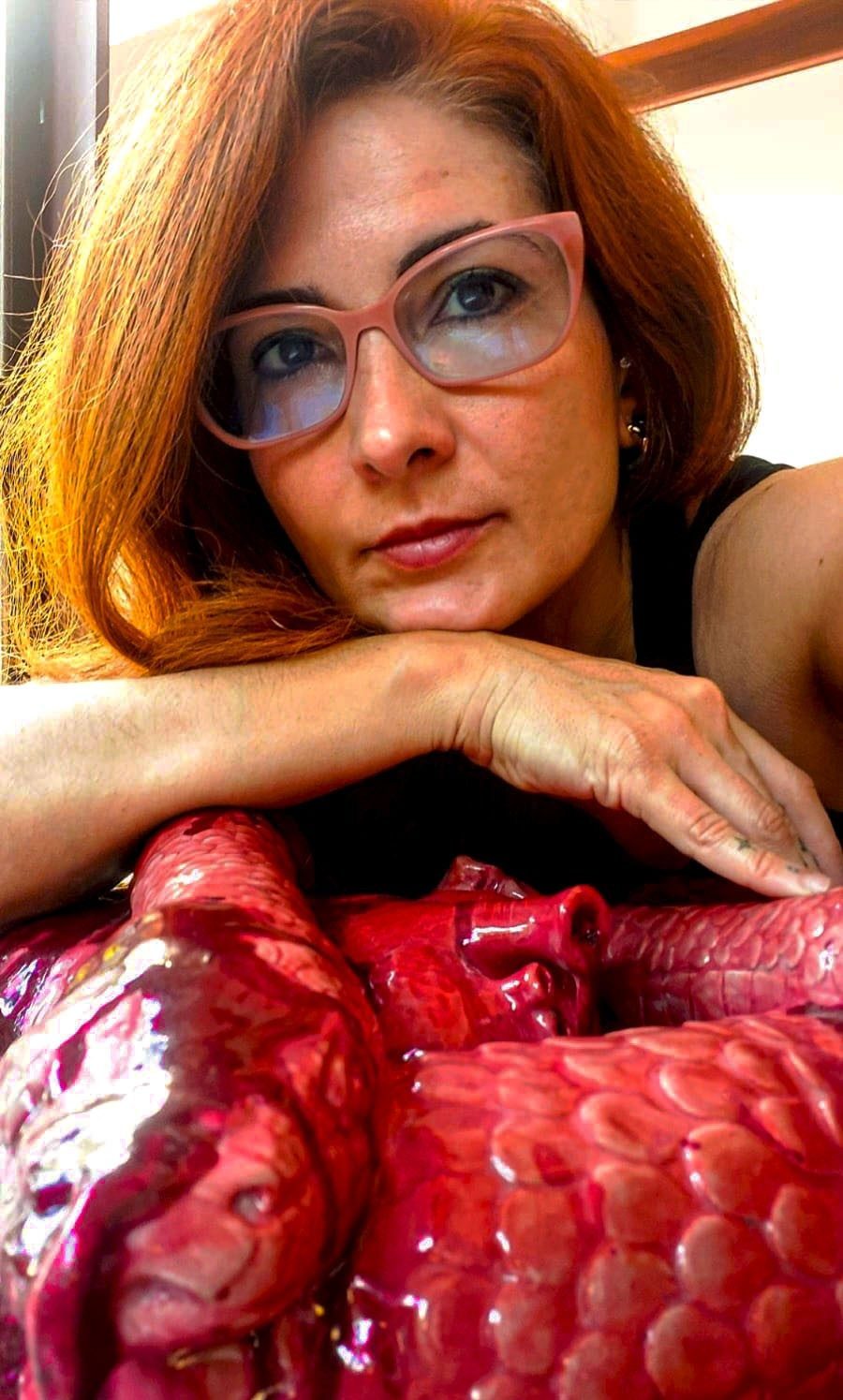 Flavia Martins Moraes apoiada sobre uma escultura de cobra em porcelana esmaltada de vermelho.